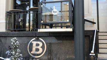 Entrada de un hotel con un letrero de accesibilidad para sillas de ruedas, un área exterior cubierta de nieve y un llamativo logotipo 'B' en la pared.