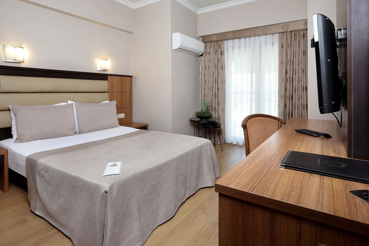 Habitación de hotel con cama, mesita de noche, escritorio, silla, televisor y aire acondicionado.