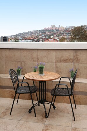Una mesa de madera redonda con cuatro sillas, dos plantas en macetas y una vista de la ciudad al fondo.