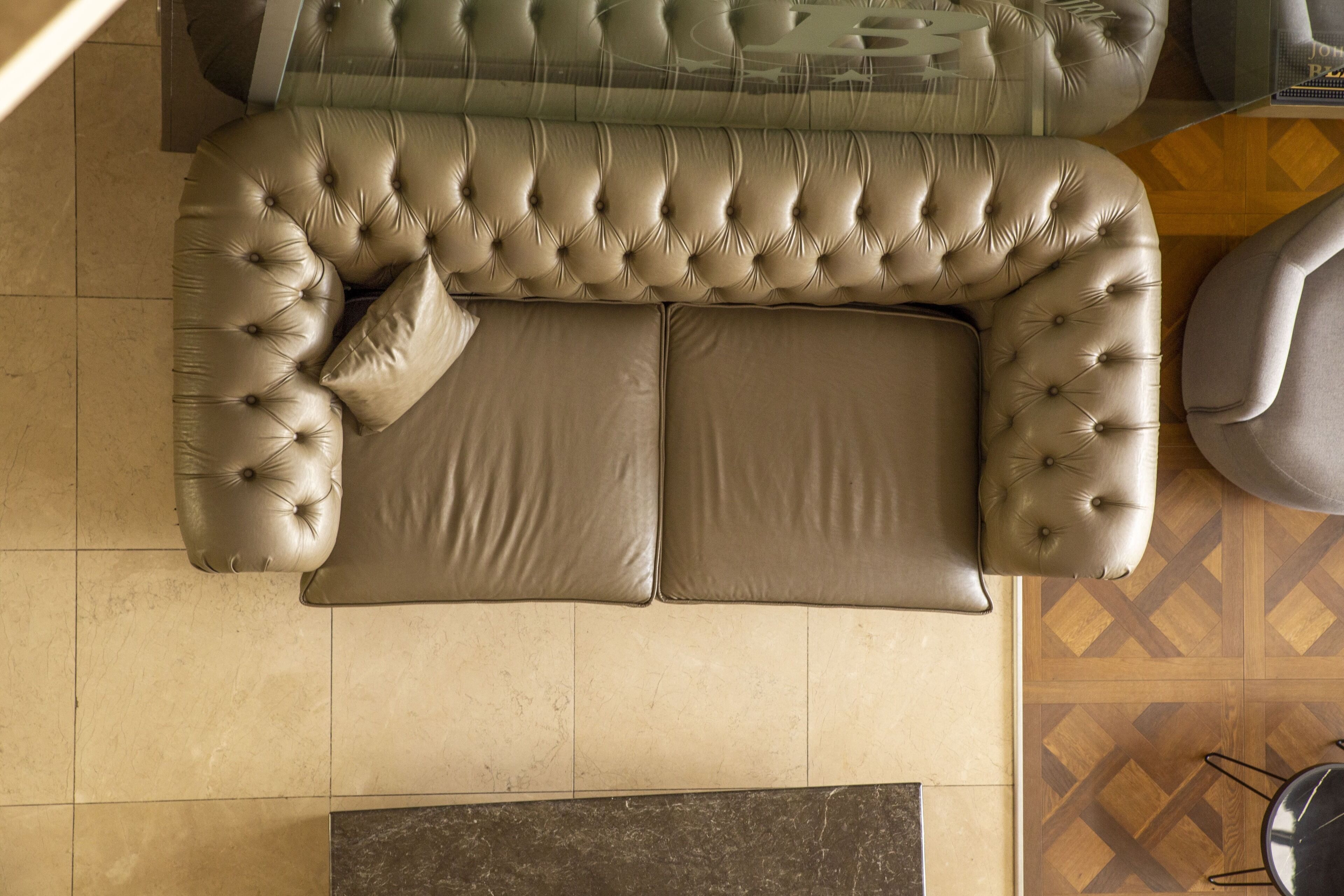 A beige tufted sofa with two cushions, a patterned rug, and a wooden floor with a geometric design.