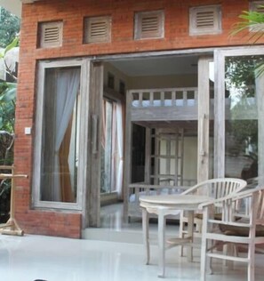 A building with a glass door leading to an outdoor seating area with a table and chairs. - Alam Pracetha Bali (Ubud)