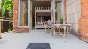 A rustic building with a large wooden door, a balcony, and a table with chairs and a potted plant. - Alam Pracetha Bali (Ubud)