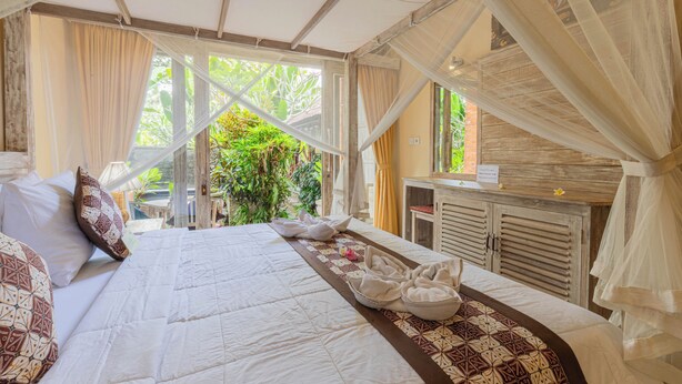 A spacious bedroom with a large bed, a wooden cabinet, and a view of greenery outside. - Alam Pracetha Bali (Ubud)