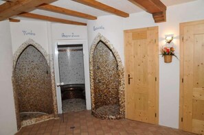A hallway with mosaic-tiled arches labeled 'Ninbeia' and 'Baqno Furoo', wooden doors, and a wall-mounted light fixture with a basket of flowers. - Hotel Ciamol (Mazzin)