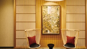 Een kamer met twee houten stoelen met zwarte kussens en rode kussens, een groot abstract schilderij aan de muur, en een houten paneeldecoratie.