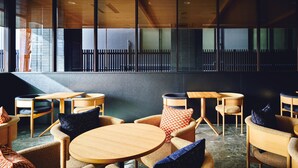 Een modern café met ronde houten tafels en rieten stoelen, met een uitzicht op een stadslandschap door grote ramen.