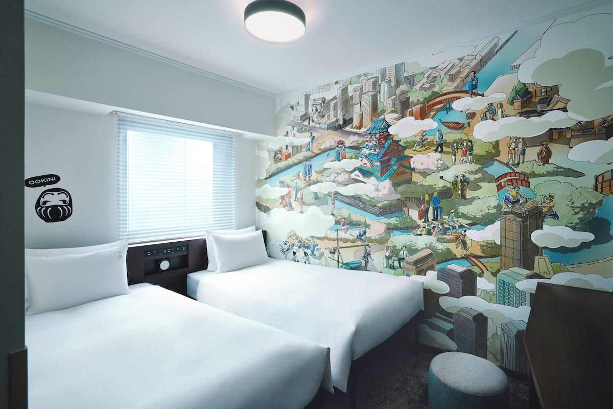 Een hotelkamer met twee bedden, een groot muurdecoratie met een stadsbeeld, en een raam met zonwering.