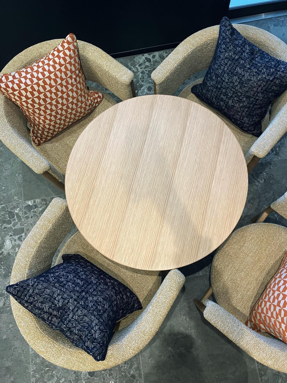 A round wooden table surrounded by wicker chairs with patterned cushions.