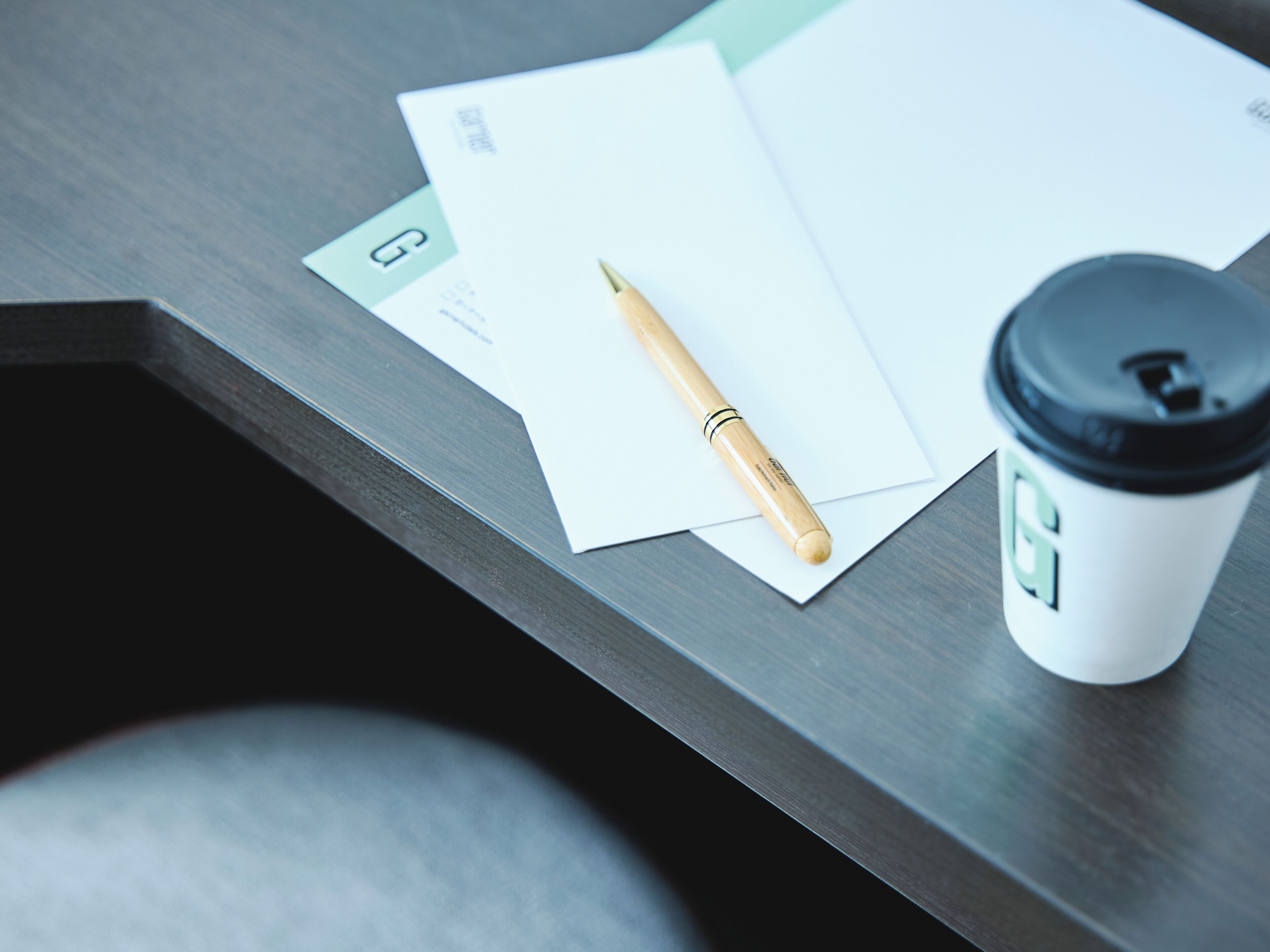 A wooden desk with a pen, a coffee cup, and some papers.