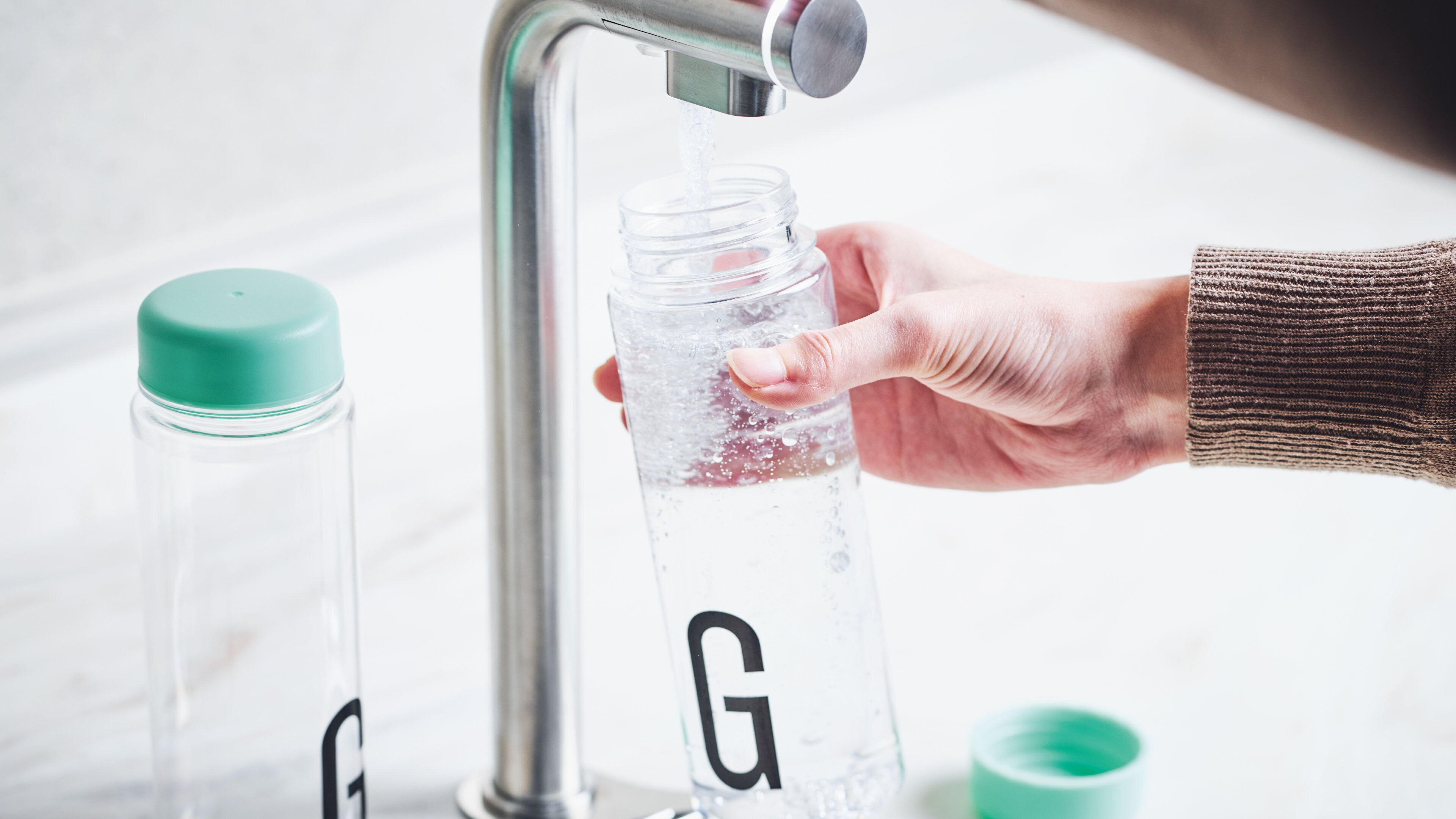 A hand filling a clear water bottle with water from a faucet.