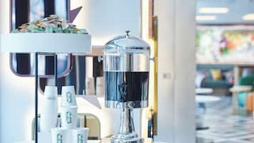 A coffee station with a coffee machine, cups, and a decorative item on a white table.