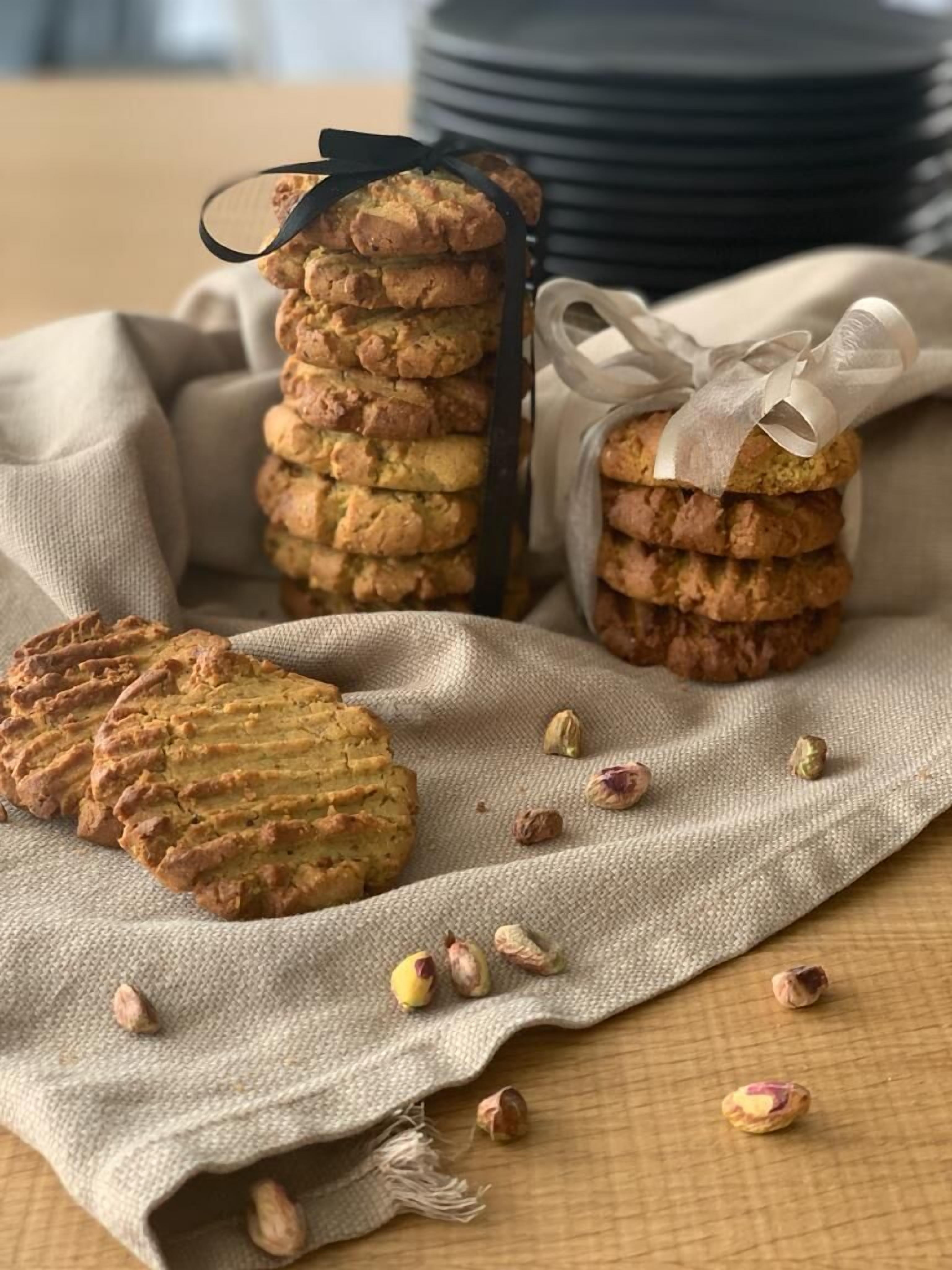 A stack of cookies and a single cookie on a cloth, with some nuts scattered around.