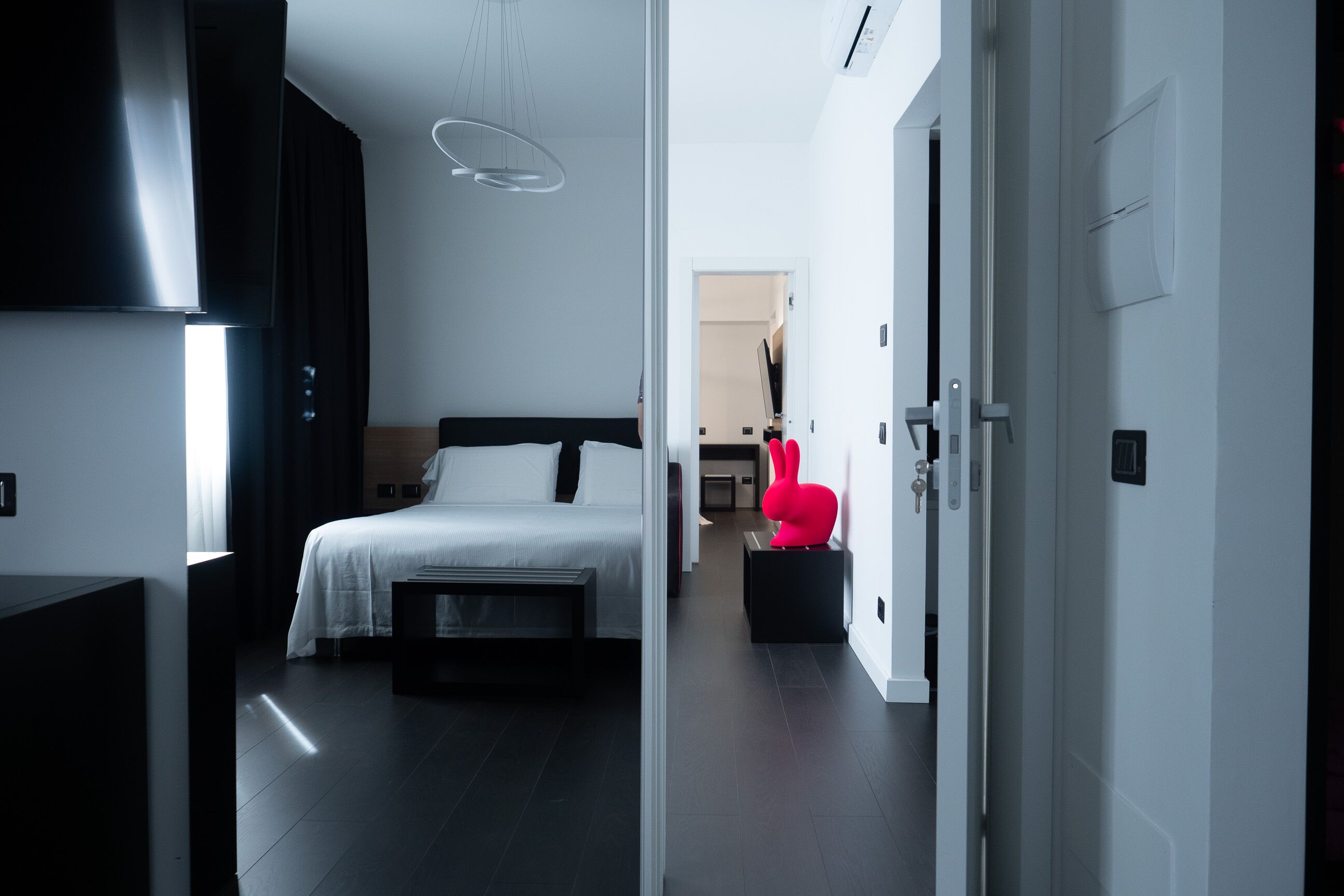 Et moderne hotelværelse med en stor seng, et lille skrivebord og en lys gang, der fører til et badeværelse.