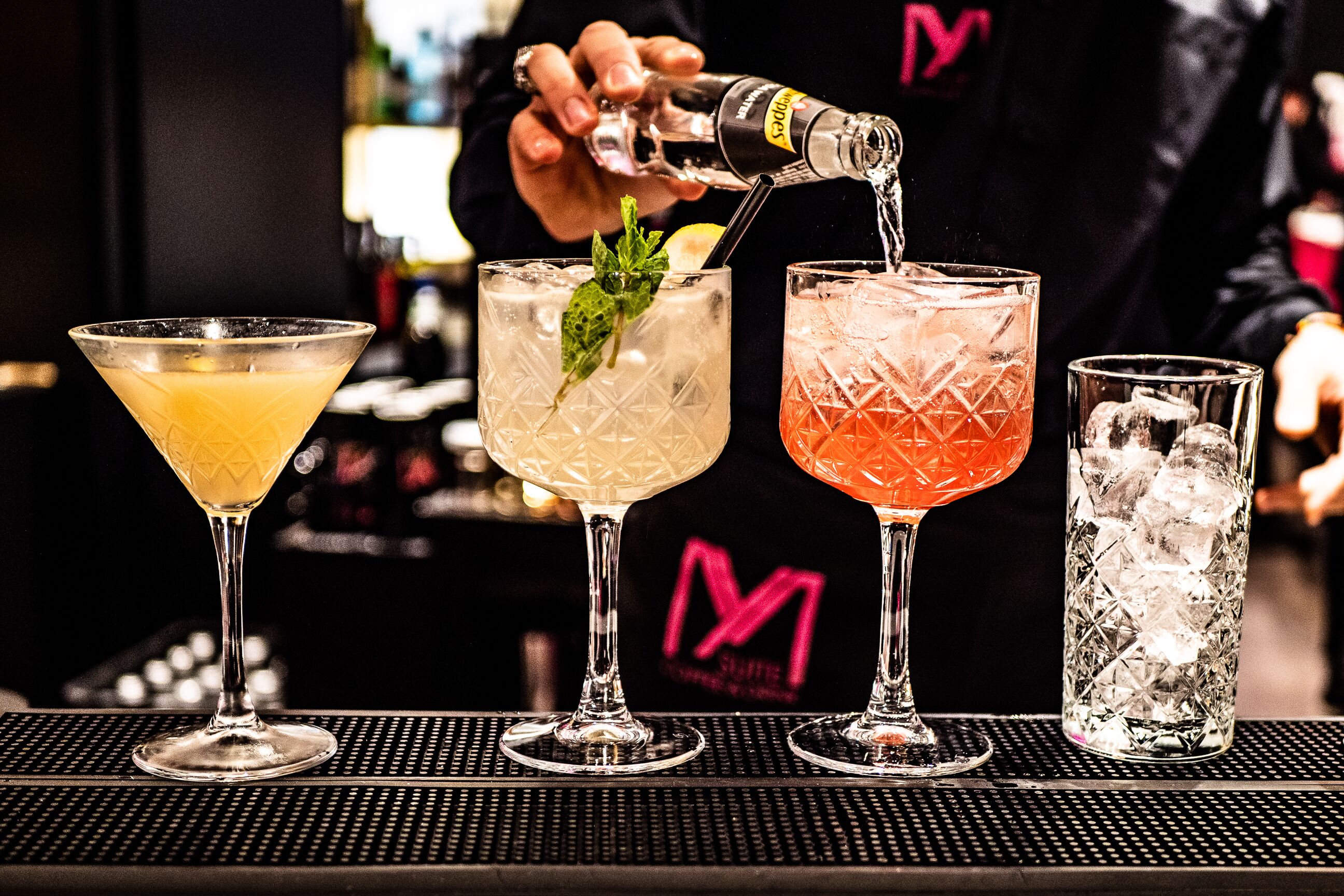 Eine Bar mit drei verschiedenen Cocktails in Martini-Gläsern und einem hohen Glas mit Eis.