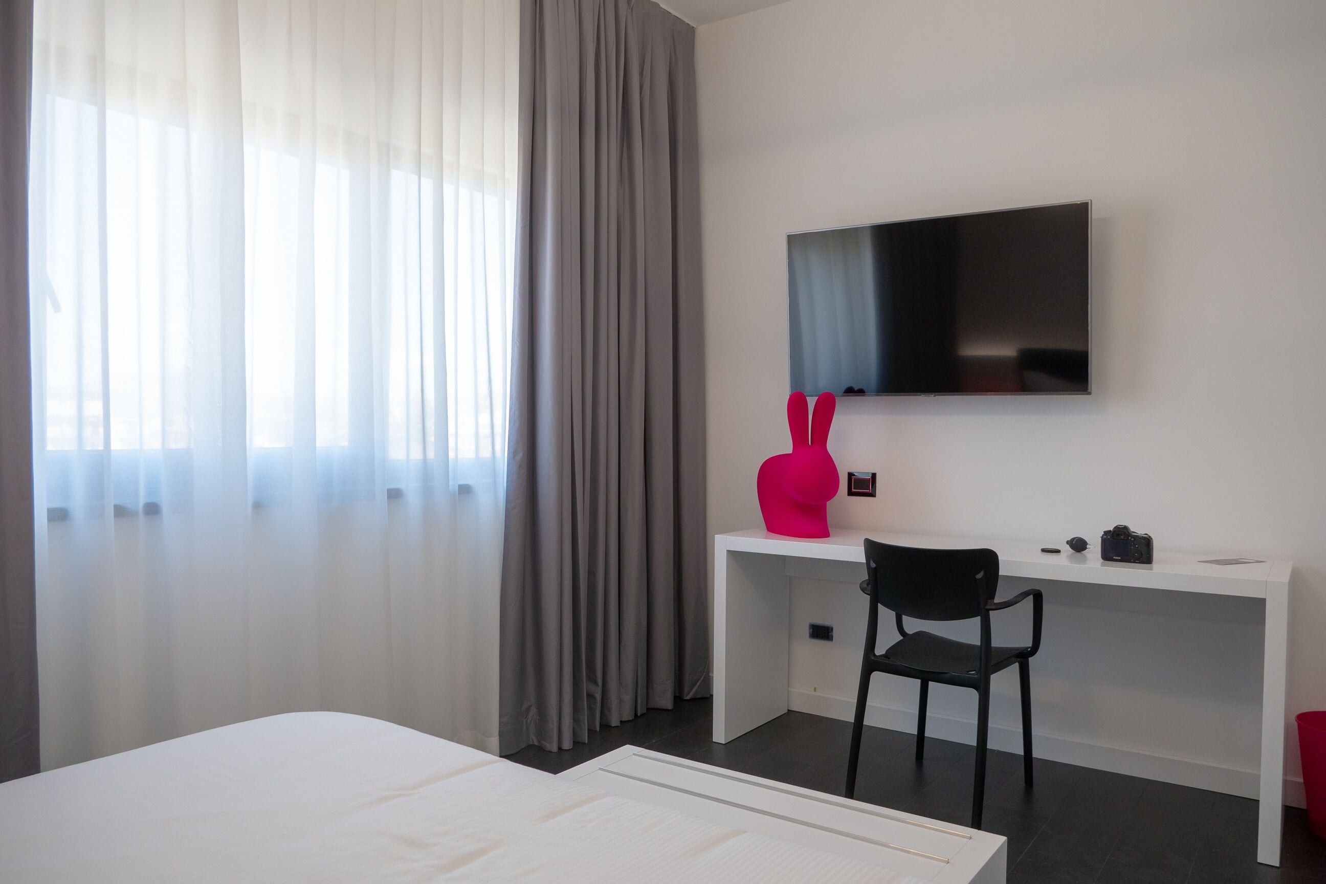Hotelkamer met een bed, een bureau met stoel, een aan de muur bevestigde televisie en een raam met gordijnen.