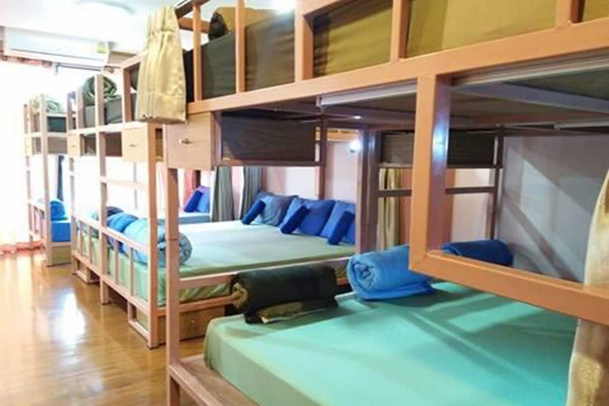 A row of bunk beds with green bedding and blue pillows, wooden frames, and storage compartments above each bed.