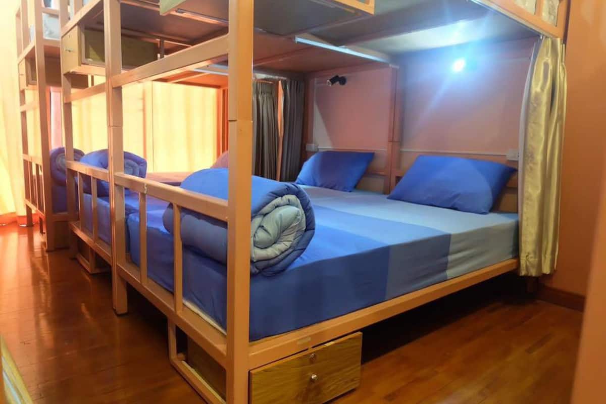 A bunk bed room with a wooden floor, a small drawer under the bed, and a curtain on the window.
