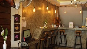 A bar area with a counter, bar stools, a fan, and a small table with a vase of flowers. - T2B Home - Adults Only - Hostel (Chiang Mai)