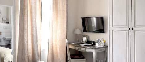 Una habitación de hotel con una cama, un escritorio con silla, un televisor y un armario.