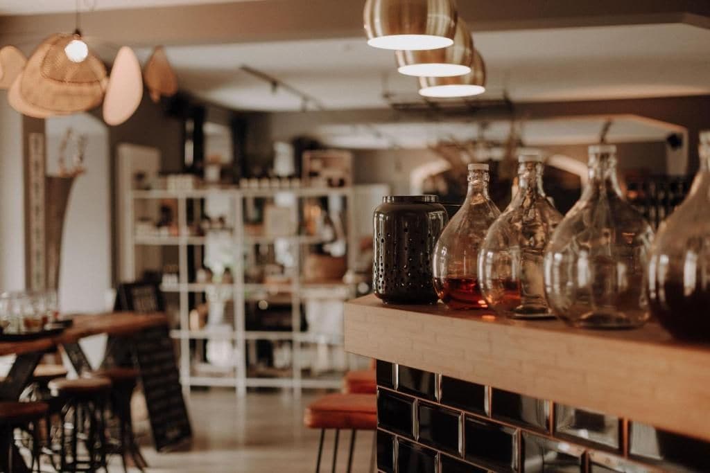 Zona de bar con luces colgantes, estanterías con botellas y una barra con vasos.