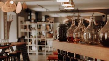 Zona de bar con luces colgantes, estanterías con botellas y una barra con vasos.