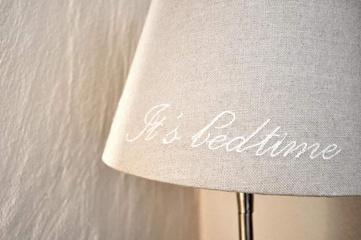 Eine Lampe mit Stoffschirm, auf dem "It's bedtime" aufgestickt ist.