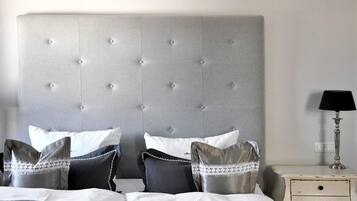 A neatly made bed with a grey tufted headboard, white and grey pillows, and a bedside table with a lamp.