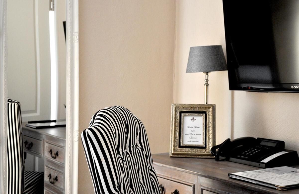 A hotel room with a desk, a framed certificate, a lamp, a telephone, and a television.