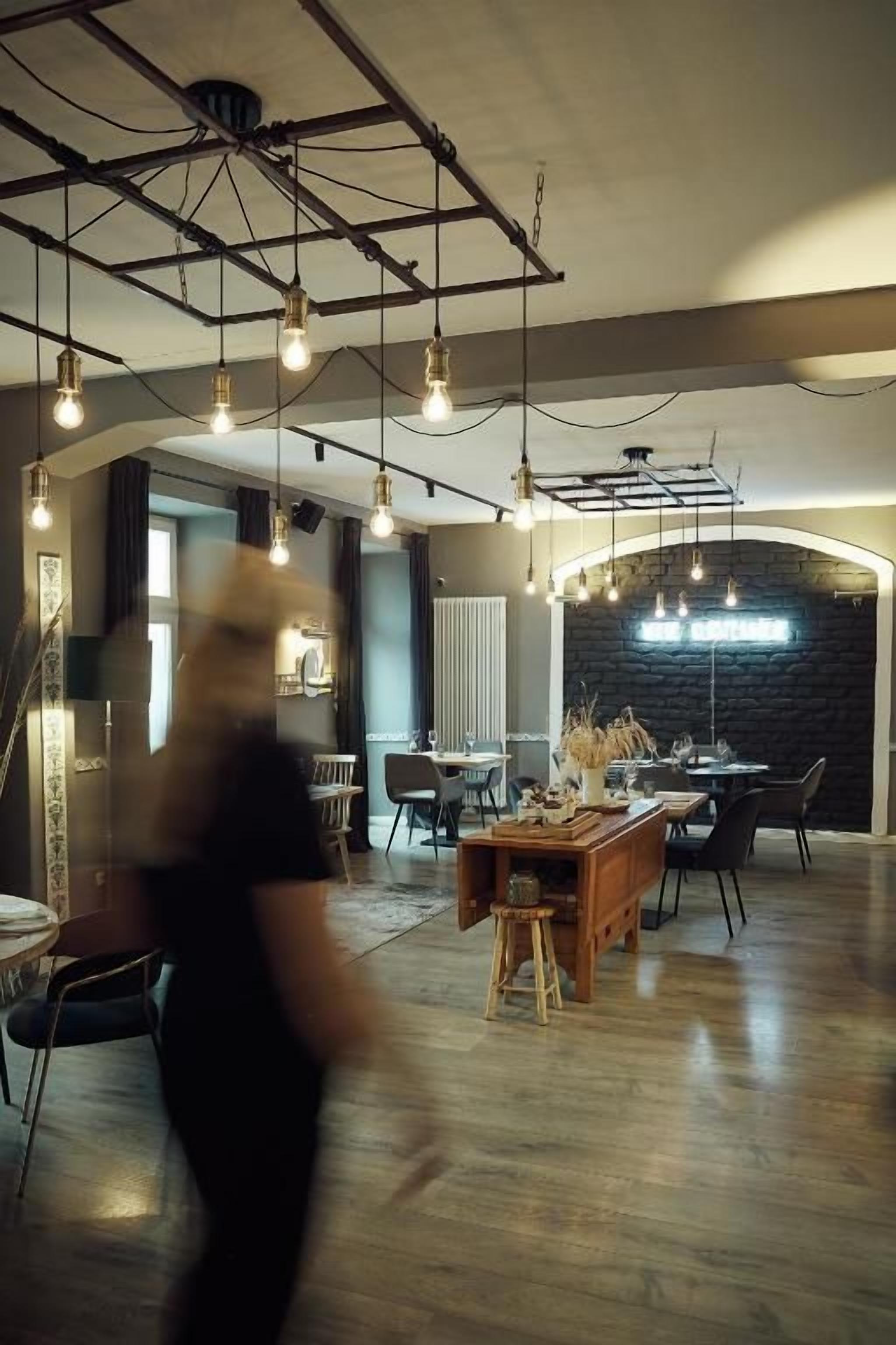 Ein modernes Interieur mit sichtbaren Balken, hängenden Leuchten und einem zentralen Essbereich mit einem Holztisch und Stühlen.