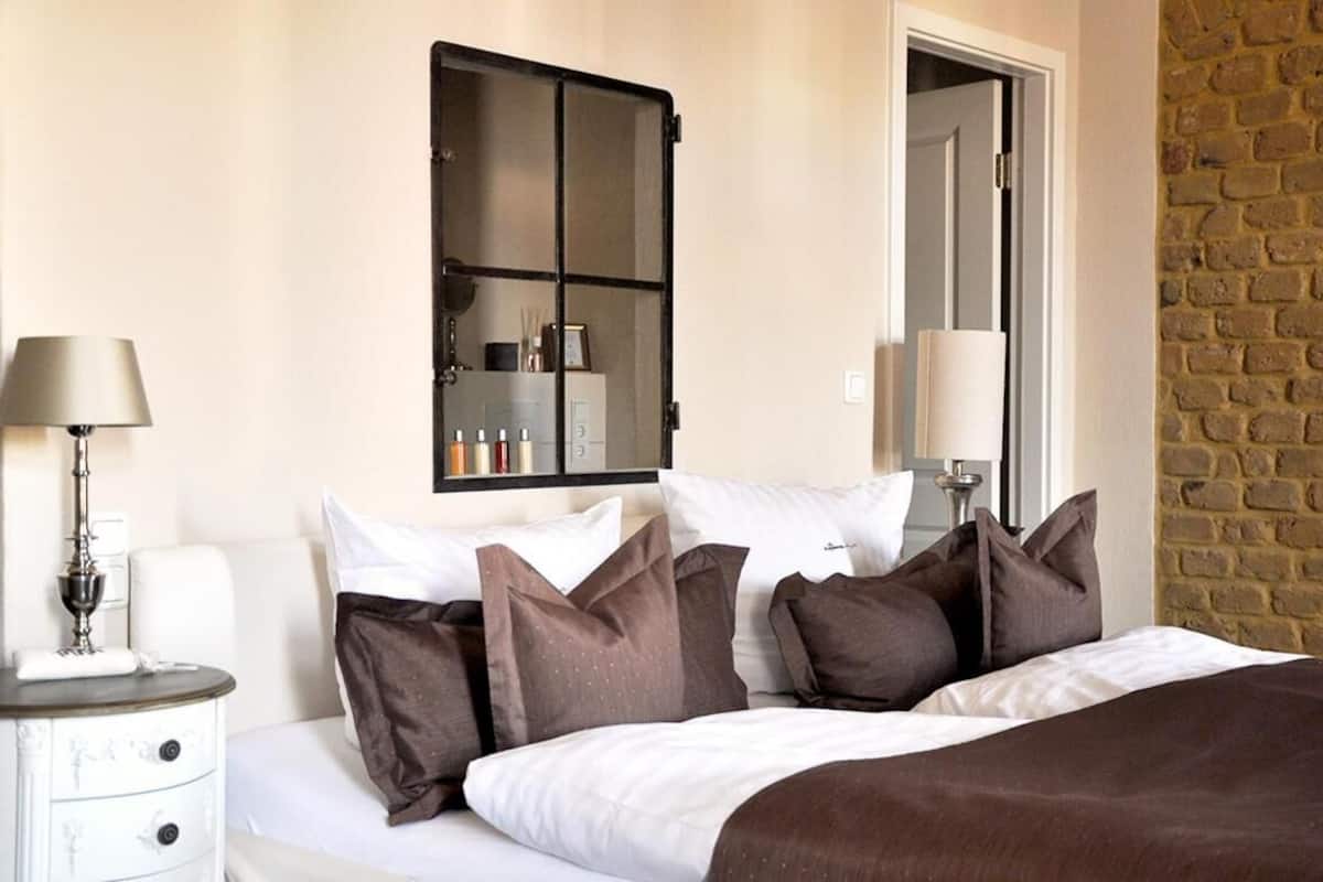 Ein Hotelzimmer mit einem Bett, einem Nachttisch mit Lampe, einem Spiegel und einer Ziegelwand.