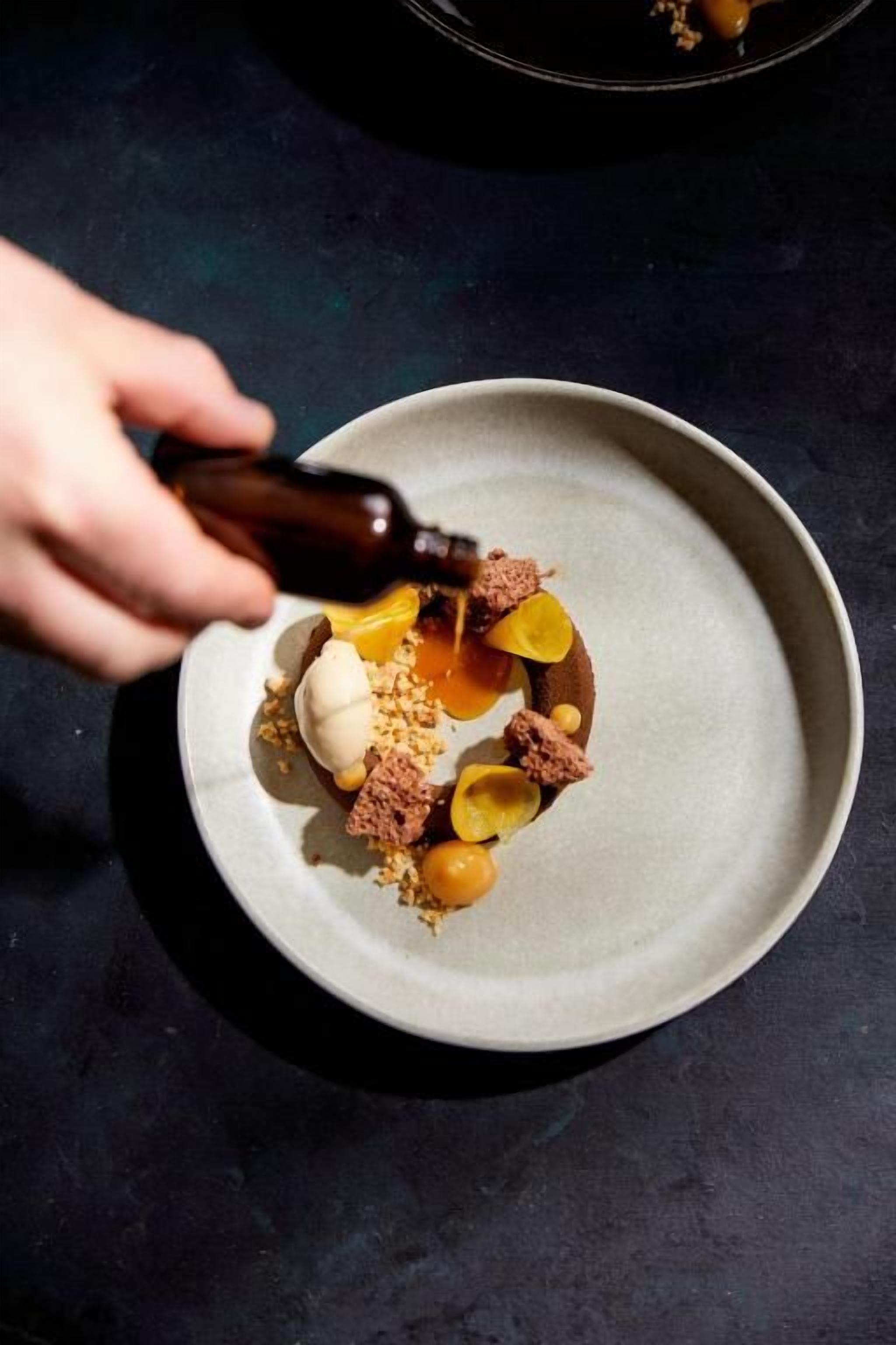 Una mano vertiendo un líquido oscuro sobre un postre en un plato.