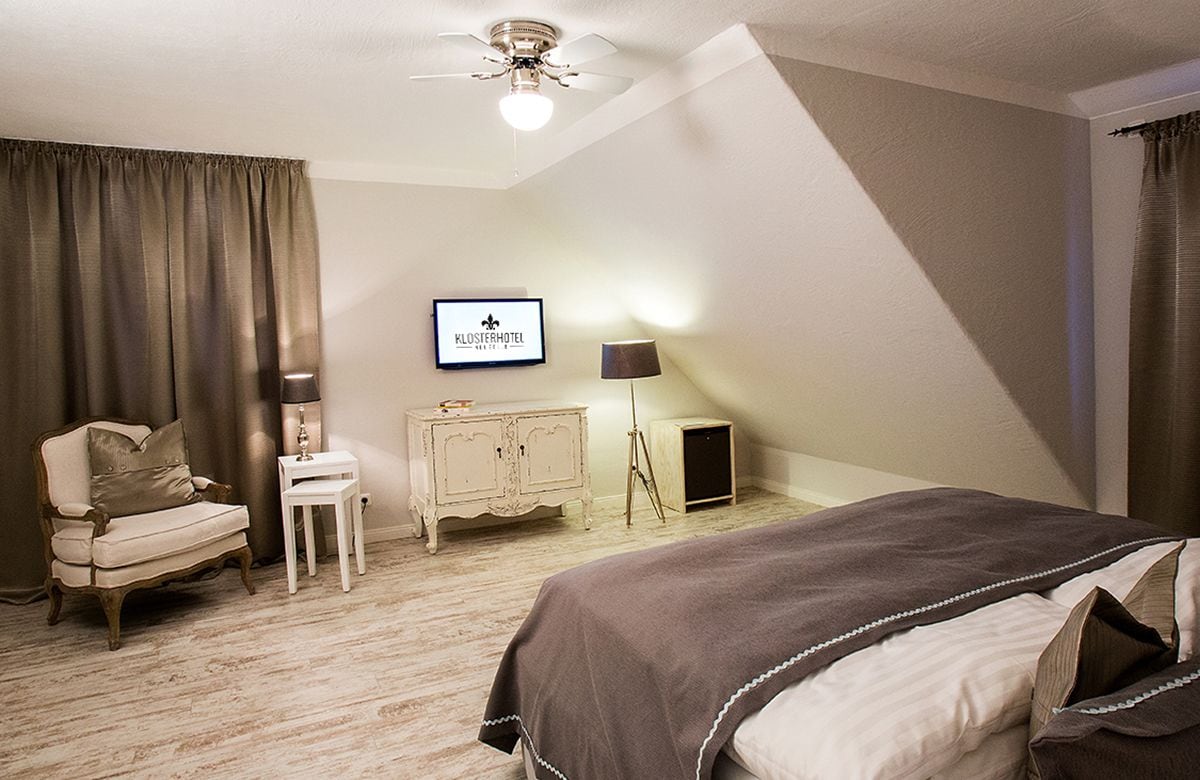 Ein Hotelzimmer mit einem Bett, einem Sessel, einem kleinen Tisch, einem Schrank und einem Fernseher an der Wand.