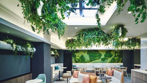 Un espace intérieur moderne doté de coins salon, de tables et d’un grand mur végétal.
