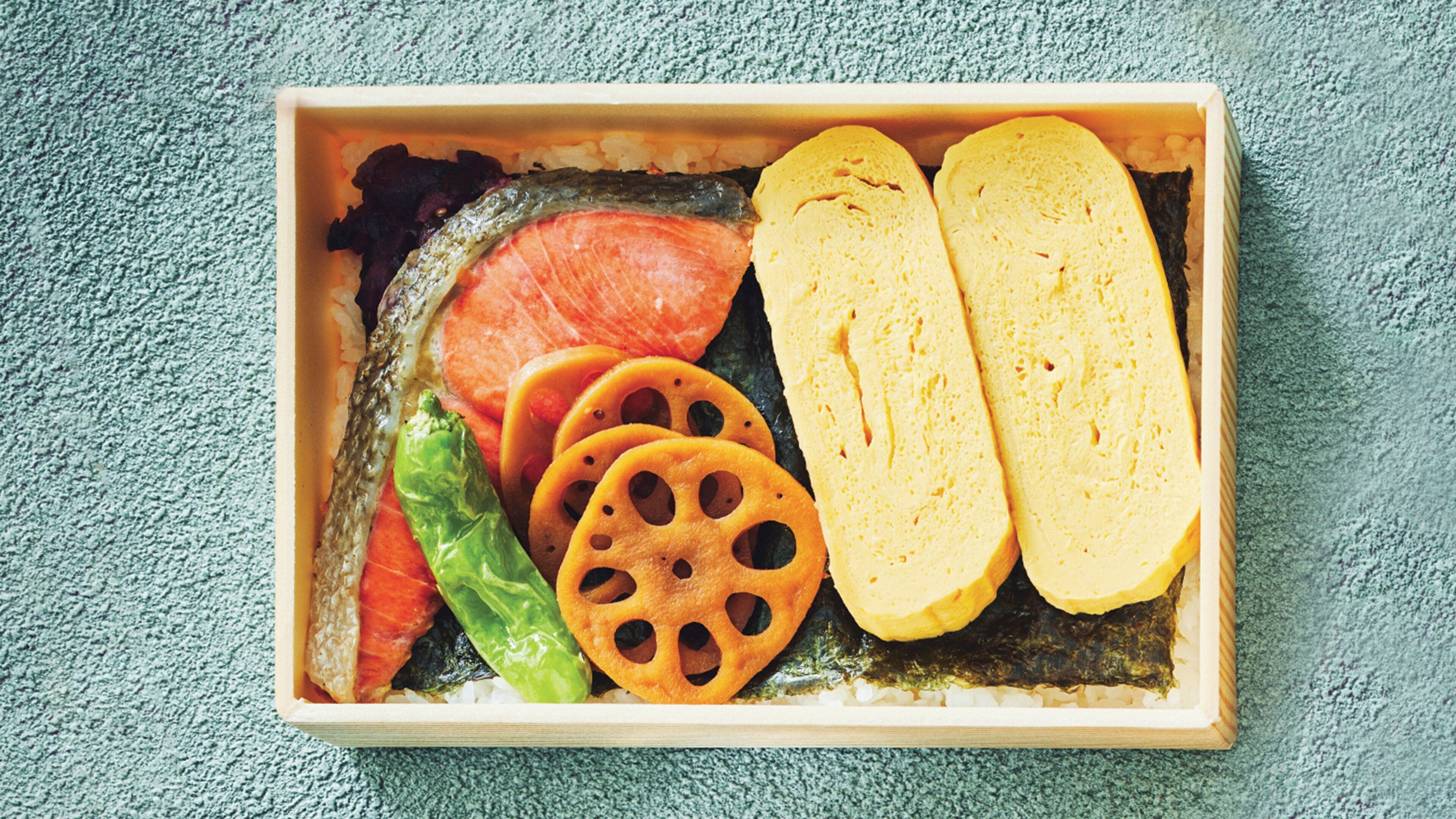 A rectangular wooden tray containing sushi, including slices of salmon, a green leaf, and two pieces of yellow bread.