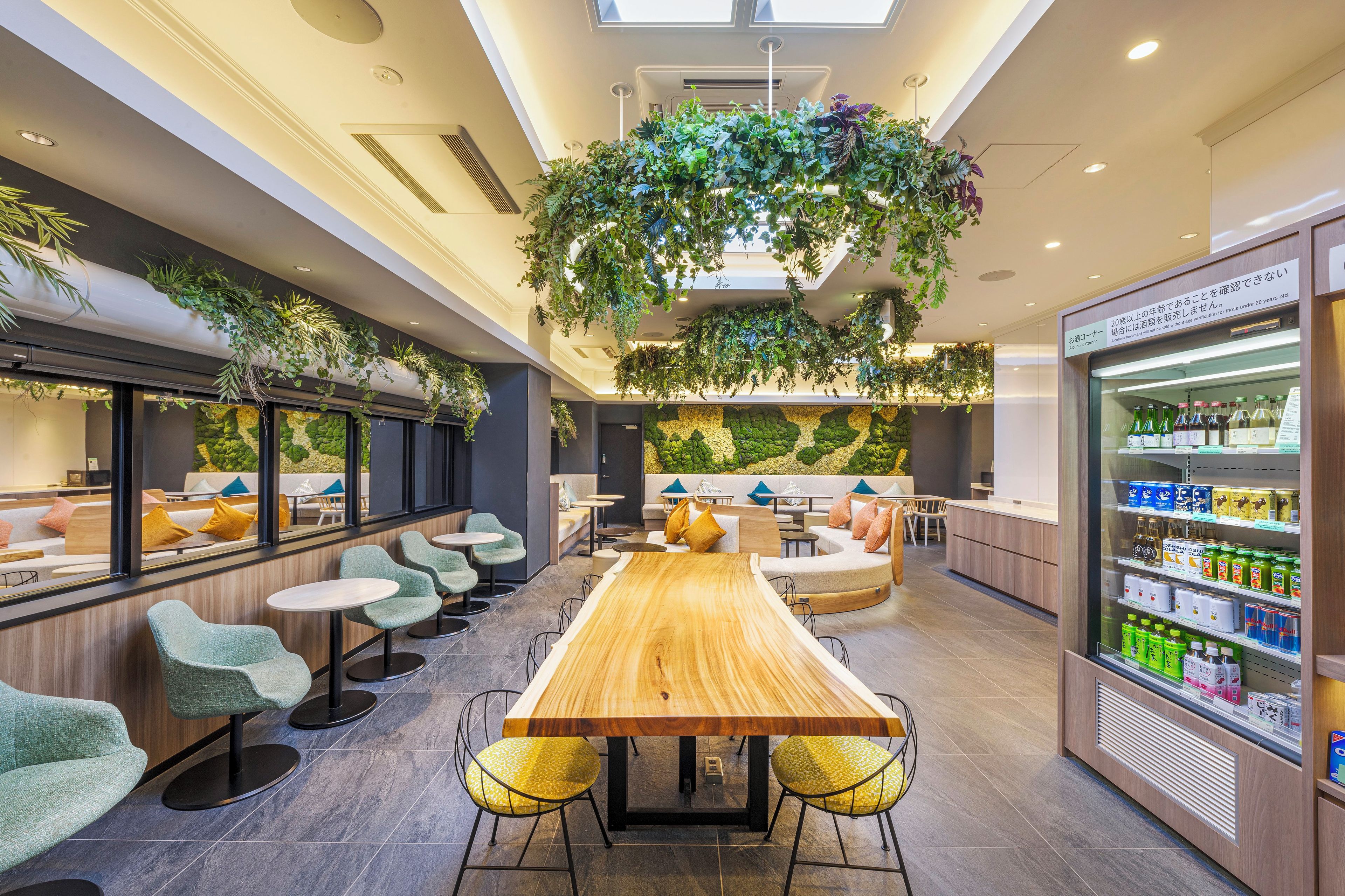 A modern lounge area with a long wooden table, multiple seating options, and a wall-mounted plant display.
