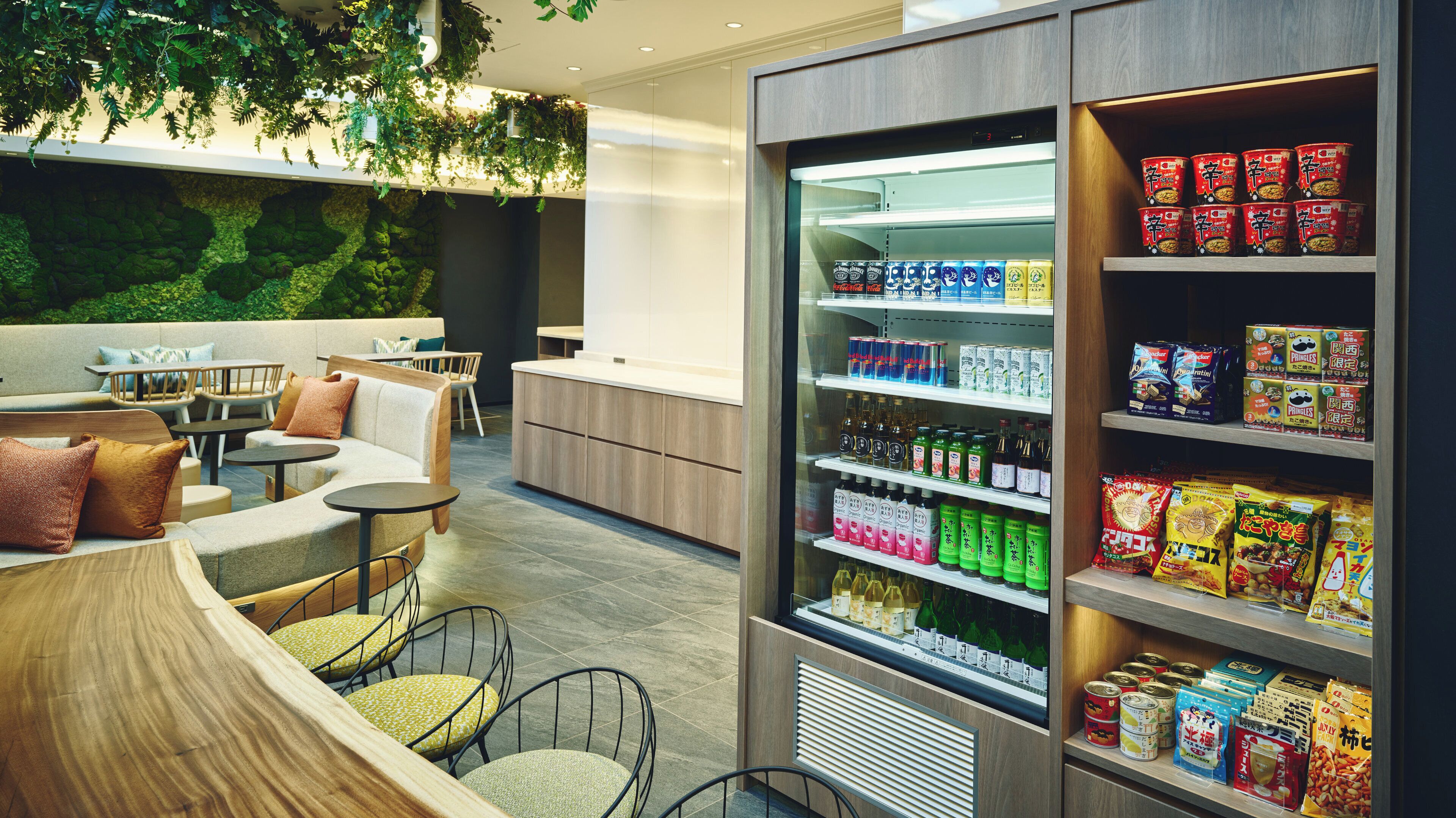 A modern lounge area with seating, a beverage vending machine, and a wall with greenery.
