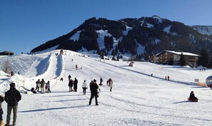 A ski slope with skiers and snowboarders, a lodge, and a mountain backdrop.