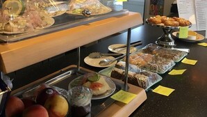 Buffet amb diferents plats, incloent fruita, pastissos i plats tapats, exposats a un mostrador amb preus indicats.