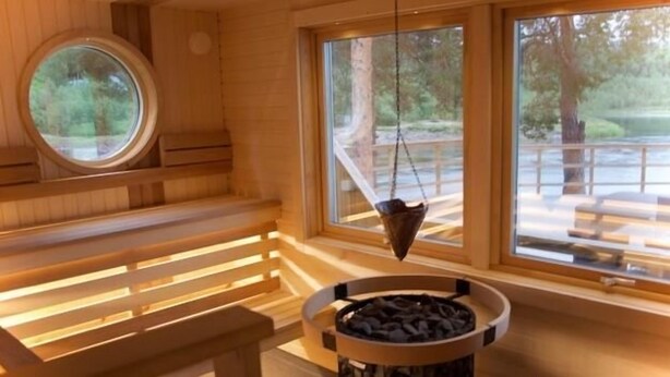 Una sauna amb bancs de fusta, una fornícula central i grans finestres que donen vistes a l'exterior.