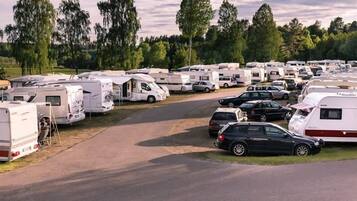 A campground with RVs and cars parked along a paved road, surrounded by trees.