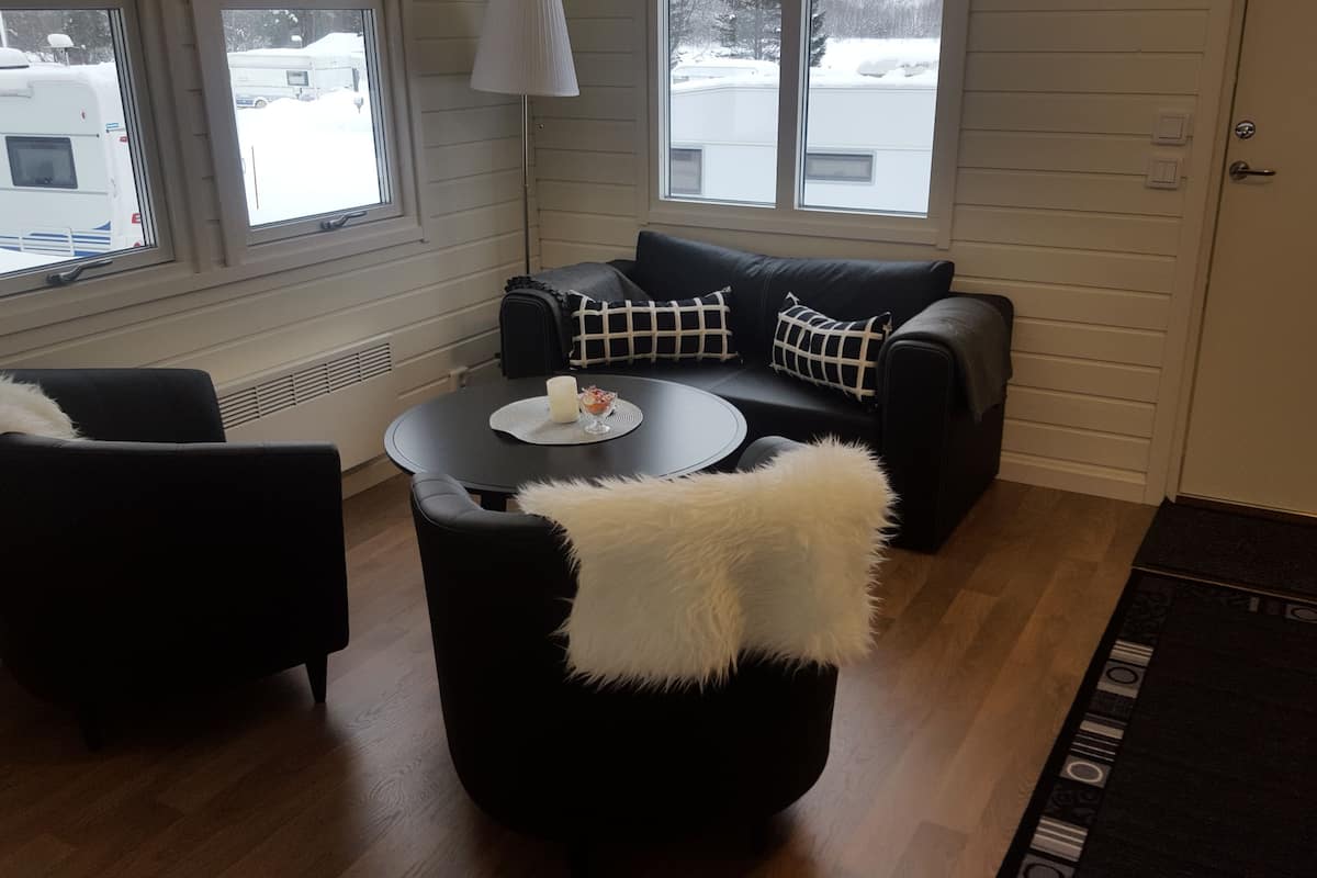Una habitación acogedora con un sofá de cuero negro, una mesa redonda con una vela y vistas a un paisaje nevado a través de ventanas amplias.