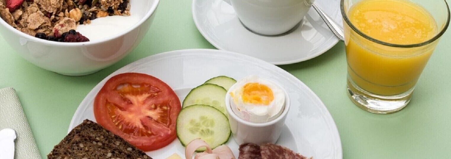 A breakfast setting with a bowl of cereal, a plate with a tomato, cucumber, and egg, a glass of orange juice, and a cup of coffee.