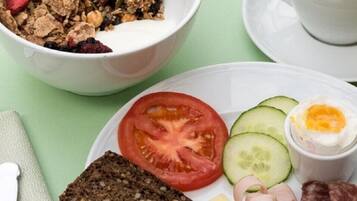 A breakfast setting with a bowl of cereal, a plate with a tomato, cucumber, and egg, a glass of orange juice, and a cup of coffee.