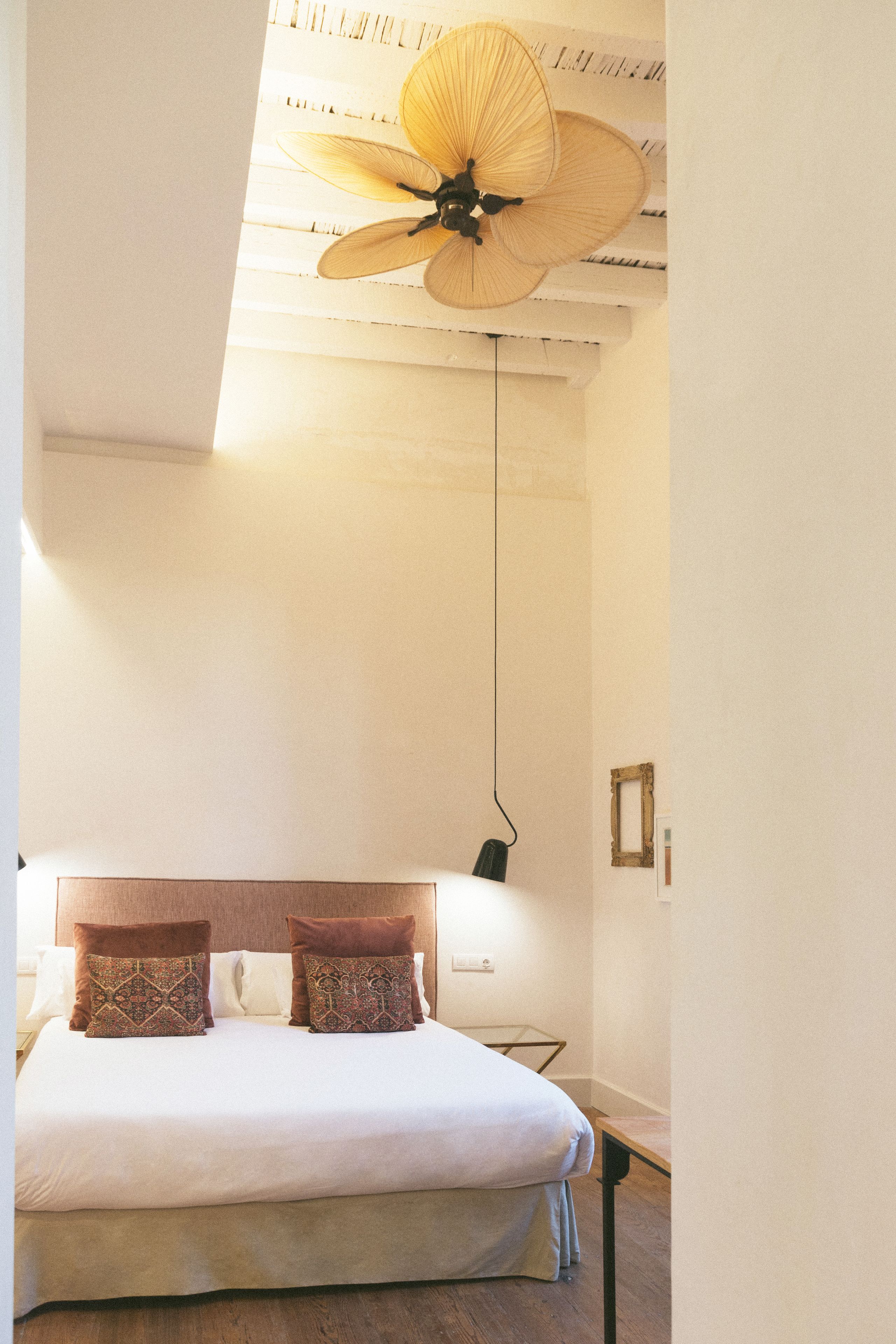 A bedroom with a bed, two patterned pillows, a ceiling fan, and a bedside table with a lamp.