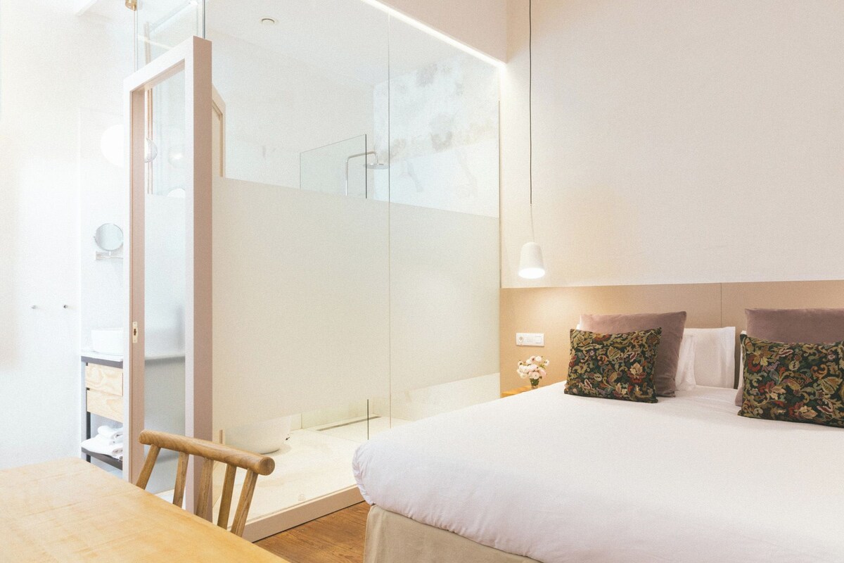 Ein Hotelzimmer mit Bett, Holztisch und Duschkabine aus Glas.