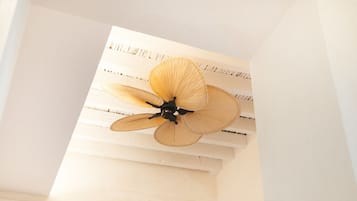 Um ventilador de teto com quatro hélices em um quarto com paredes brancas e teto inclinado.