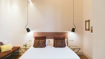 Un dormitorio ordenado con una cama grande, dos mesitas de noche, un banco y un aplique de pared.