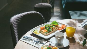 Un desayuno con tostadas, una taza de café y un vaso de jugo de naranja sobre una mesa de madera.
