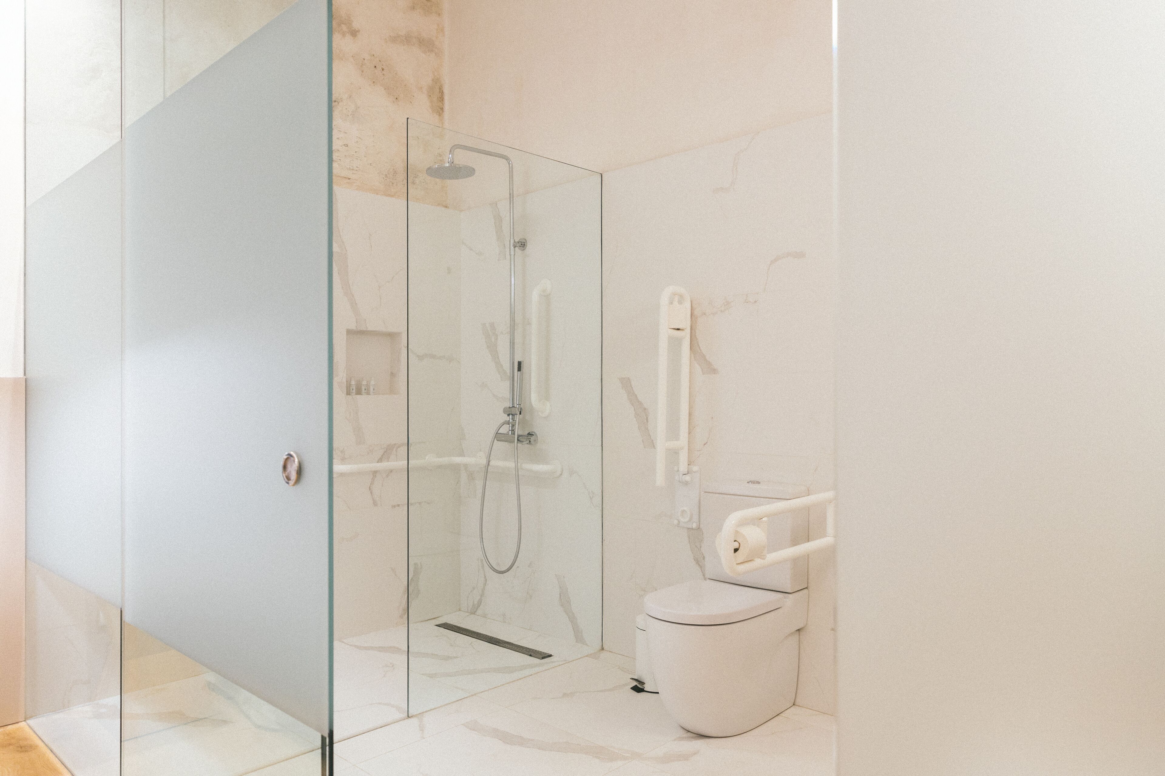 Un baño moderno con cabina de ducha de vidrio, inodoro blanco y suelo de mármol.