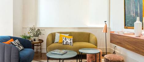 A living room with a sofa, armchair, coffee table, ottoman, and a painting on the wall.
